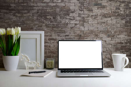 Modern workplace with laptop computer, houseplant and picture frame on white table. Blank screen for...