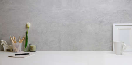 Home office interior. Picture frame, coffee cup, notebook and pencil holder on white table against. Copy space.の写真素材