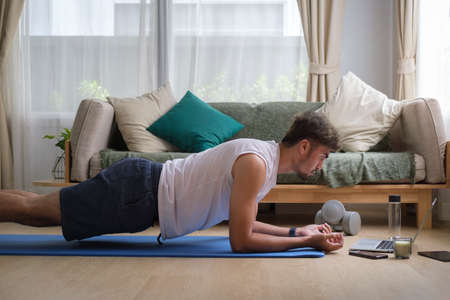 Sporty man doing yoga plank while watching online tutorial on computer laptop. Healthy lifestyle...