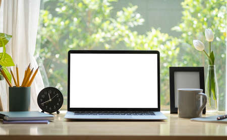 Laptop computer with blank display, coffee cup, pencil holder and picture frame on wooden table in...