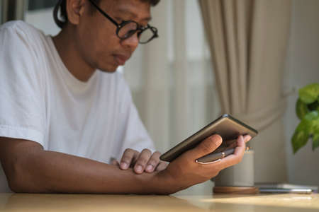 Young Asian man sitting on comfortable and using digital tablet.