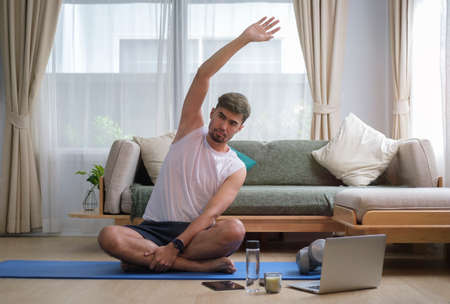 Handsome man doing sideways during warm up before workout at home. Healthy lifestyle concept.の写真素材