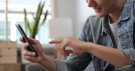 Cropped shot of happy man sitting on sofa at home and using smart phone.