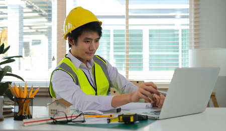 Professional Asian male architect using laptop computer, working on construction plan at his workplace.の写真素材