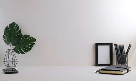 Home office desk with, stationery, picture frame and potted plant on white table. Copy space.の写真素材