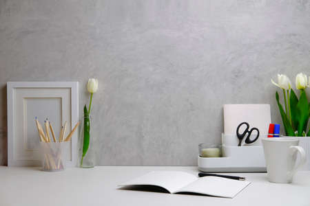 Home office interior. Picture frame, coffee cup, notebook and pencil holder on white table against. Copy space.の写真素材