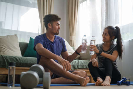 Happy young couple drinking water, resting after domestic workout at home.  Healthy lifestyle, yoga, pilates, exercising concept.の写真素材