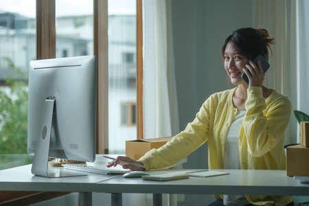 Startup small business owner receiving order on smart phone and working with computer at home...