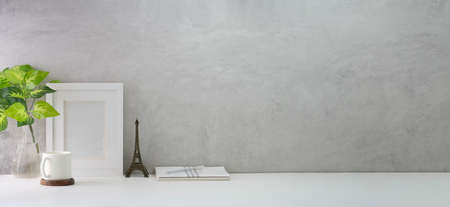 Comfortable workplace with blank picture frame, houseplant, book and coffee cup on white table against loft wall. Copy space for your text.の写真素材