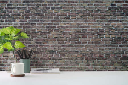 Coffee cup, houseplant and pencil holder on white table against brick wall. Copy space for your text.の写真素材