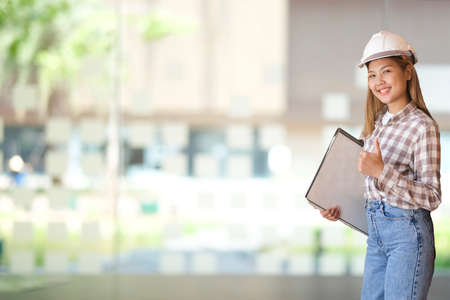 Smiling female architect in safety helmet with blueprints standing in modern office.の写真素材