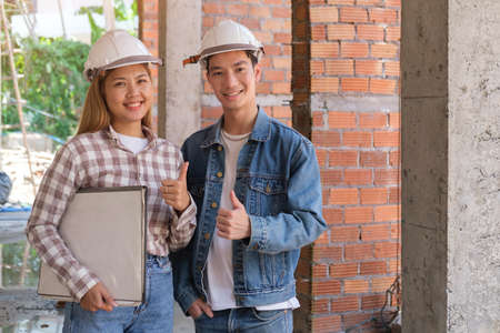 Confident architects wearing safety helmet standing at construction site and showing thumb up at camera.の写真素材