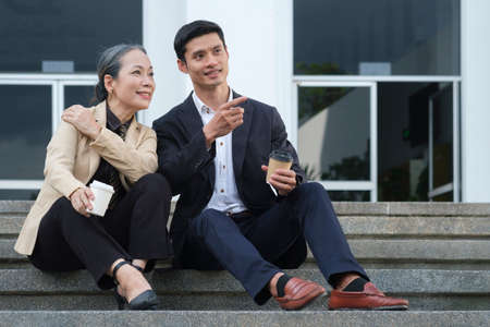 Two successful business people sitting on a stairs of an office building and talking to each other.の写真素材
