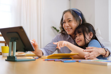 Happy grandmother watching cartoons online with her little granddaughter on tablet, enjoying free time on weekend at home together.の写真素材