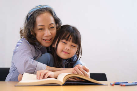 Loving senior grandmother hugging and reading fascinating fairytale to her grandchild. Family holiday and togetherness.の写真素材