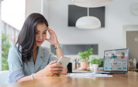 Serious female employee using mobile phone at office desk.
