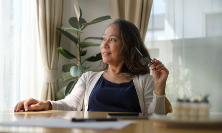 Happy mature woman sitting in comfortable home and looking thoughtfully.の写真素材