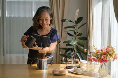 Happy middle aged woman preparing coffee for breakfast in comfortable home kitchen. Retirement, Healthy seniors lifestyle.の写真素材