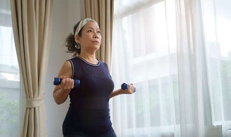 Healthy middle age lady lifting dumbbells, doing daily exercises at home. Retirement, fitness, healthy lifestyle, sport and activity concept.の写真素材