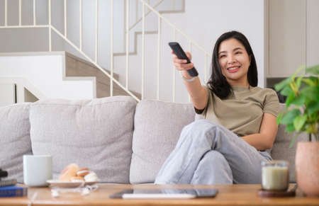 Smiling young woman sitting on comfortable sofa, enjoying watching television at home.の写真素材