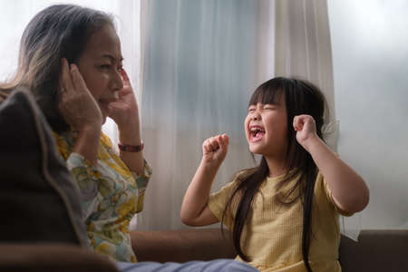 Stubborn girl in tantrum, screaming at annoyed grandmother. Negative human emotion, complicated relationships with child and family conflict concept.の写真素材