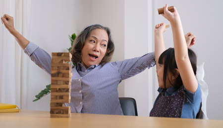 Joyful adorable little girl playing wooden blocks with grandmother in living room, spending happy time on weekend together.