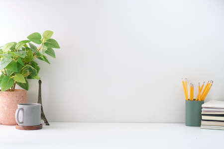 Minimal workplace with picture frame, potted plant and coffee cup on white table. Copy space for...