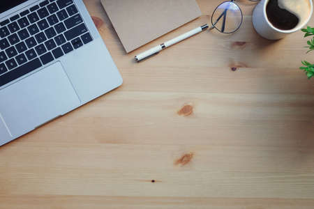 Computer laptop, eyeglasses, coffee cup and notebook on wooden desk. Top view.