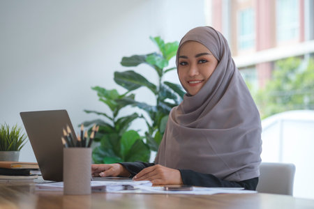 Beautiful muslim businesswoman in hijab sitting at bright modern office and smiling to camera.の写真素材