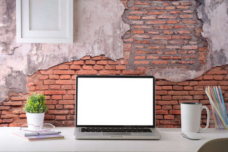 Stylish workplace with laptop computer, coffee cup, stationery and houseplant on white table against brick wall. Blank screen for your advertise text.の写真素材