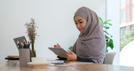 Smiling young businesswoman in hijab working in bright modern office and using modern devices.の写真素材