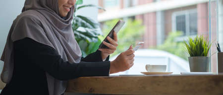Smiling muslim woman in hijab holding credit card for online shopping or payment online on smart...
