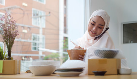 Young muslim woman in hijab confirming orders from customer on mobile phone. Small business owner, Online selling, E-commerce concept.の写真素材