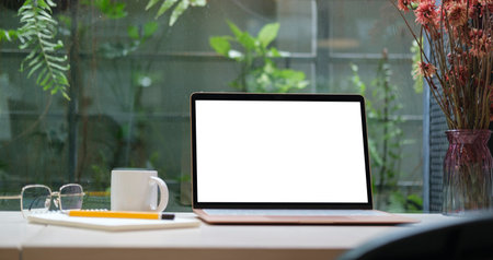 Laptop computer with blank display, eyeglasses, coffee cup and notebook on white table. Home office desk.の写真素材
