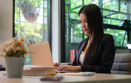 Charming young businesswoman working with laptop computer while sitting in bright modern office.の写真素材