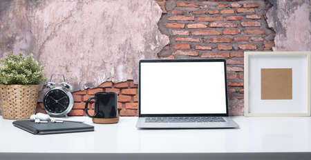 Laptop computer with blank screen, coffee cup, picture frame and potted plant on white table....