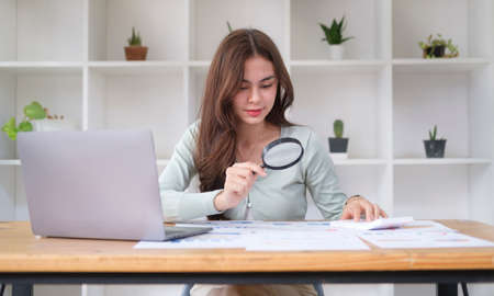 Investigator or auditor checking financial documents with magnifying glass over office desk.の写真素材