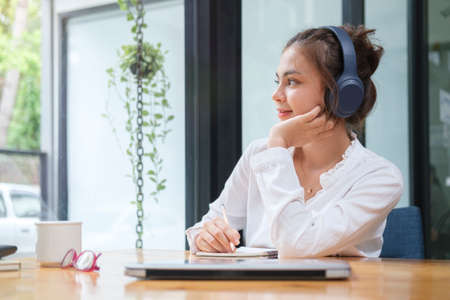 Thoughtful young woman listening music on headphone and looking out the window, enjoys view in the...