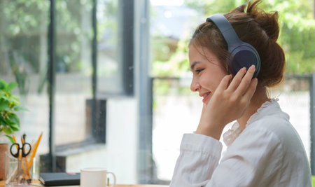 Pretty young woman listening to music with wireless headphone and relaxing at her workplace.の写真素材