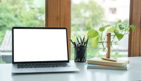 Laptop computer with white screen, books and coffee cup on wooden desk near window.の写真素材