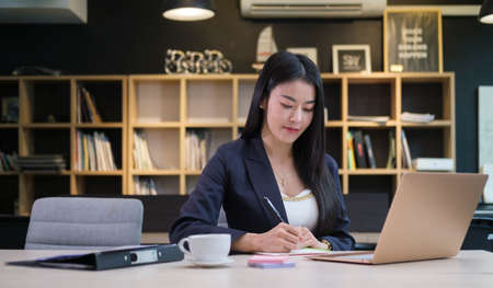 Professional businesswoman working with laptop computer and writing business plan on notepad.の写真素材