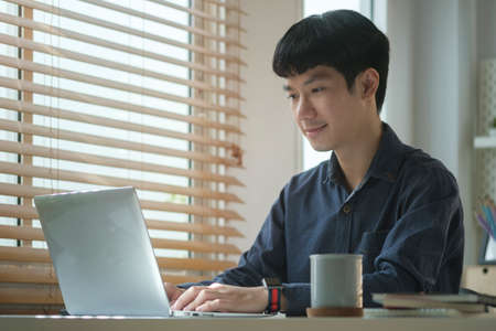 Handsome young businessman using computer laptop while sitting in bright modern office.
