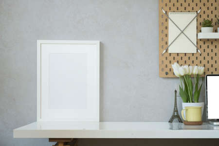 Blank picture frame, coffee cup, laptop, pencil holder and flower pot on white table.の写真素材