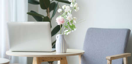 Laptop computer and vase with bouquet on round wooden table in comfortable home.の写真素材