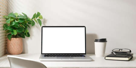 Bright modern working space with laptop, potted plant, coffee cup and notebook. White screen for your advertise text.の写真素材