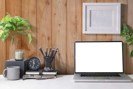 Simple workplace with laptop computer, coffee cup, houseplant and stationery on white table.