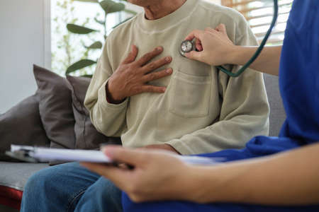 Young male doctor in white uniform holding stethoscope examining senior patient. Elderly medical...