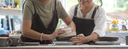 Senior female professional potter teaching young woman to make ceramic products in a pottery workshop.の写真素材