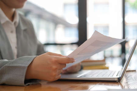 Cropped view of businesswoman holding financial and working with laptop computer at office desk.の写真素材