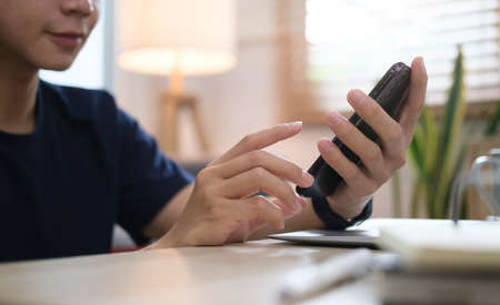 Cropped shot man in casual clothes sitting on sofa and using smart phone, checking social media,...